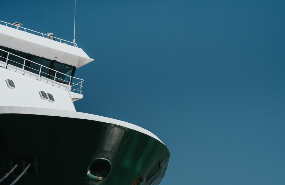 A white ship's hull against a clear blue sky. A dark green lower section features a circular opening.