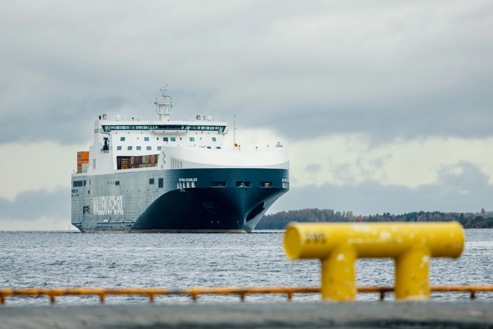 A large ferry labeled “Botnia Enabler” is sailing on a body of water under a cloudy sky. Yellow bollards are visible in the foreground.